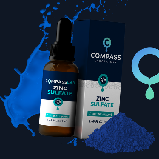 An amber glass dropper bottle and matching box of Compass Laboratory Zinc Sulfate immune support supplement, styled with blue liquid splashes and a pile of blue powder on a dark background.